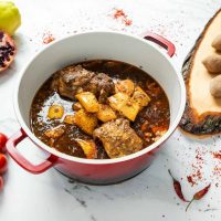 Catering Berlin Quitten-Eintopf mit Fleisch in einem roten Topf, serviert mit Reis oder Kibbeh auf einem Holzbrett.