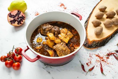 Catering Berlin Quitten-Eintopf mit Fleisch in einem roten Topf, serviert mit Reis oder Kibbeh auf einem Holzbrett.