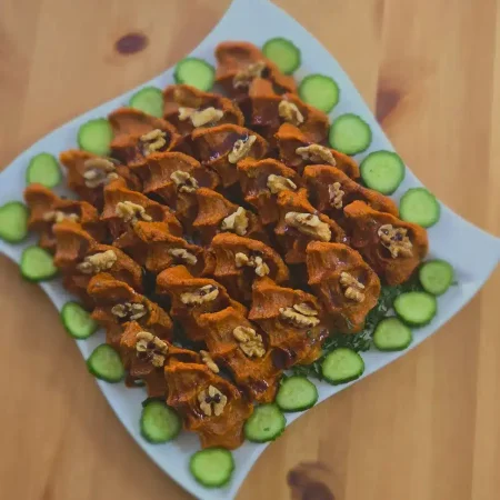 Ein stilvoll angerichteter Teller mit Kubba, verfeinert mit Granatapfelsaft, Walnüssen und frischen Gurkenscheiben.