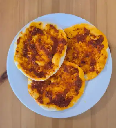 Drei Fatayer mit Paprikapaste auf einem weißen Teller, serviert auf einem Holztisch.