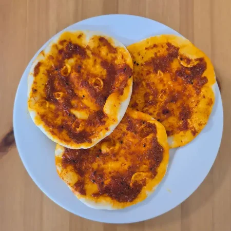 Drei Fatayer mit Paprikapaste auf einem weißen Teller, serviert auf einem Holztisch.