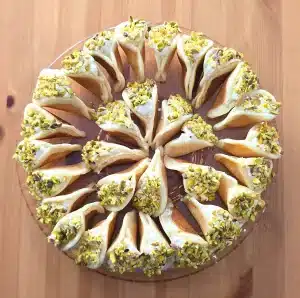 Katayef mit Sahnefüllung, dekoriert mit Pistazien, serviert auf Glasplatte – orientalisches Dessert vom Aleppo Al Shahba Catering