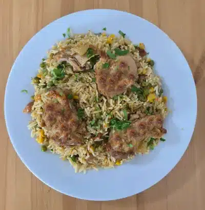 Ein Tablett mit gebratenem Hähnchen und Reis, garniert mit einer Mischung aus gerösteten Nüssen wie Pistazien, Cashews und Mandeln, sowie Zitronenscheiben und frischem Salat als Dekoration.