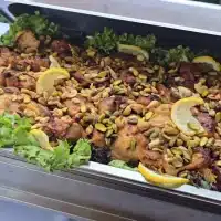 Orientalisches Reisgericht mit Hähnchen, gerösteten Nüssen und Zitronenscheiben in einer Edelstahl-Cateringform, garniert mit frischem Salat.