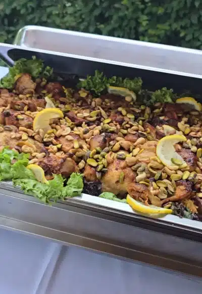Orientalisches Reisgericht mit Hähnchen, gerösteten Nüssen und Zitronenscheiben in einer Edelstahl-Cateringform, garniert mit frischem Salat.