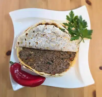 Frisch gebackenes Hackfleisch (Lahm bi Ajeen) – dünner Teig belegt mit würzigem Hackfleisch, Petersilie und Tomaten, angerichtet auf grünem Salat.