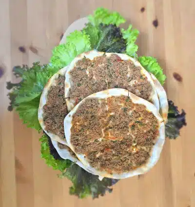 Teigfleisch Frisch gebackenes Hackfleisch (Lahm bi Ajeen) – dünner Teig belegt mit würzigem Hackfleisch, Petersilie und Tomaten, angerichtet auf grünem Salat.