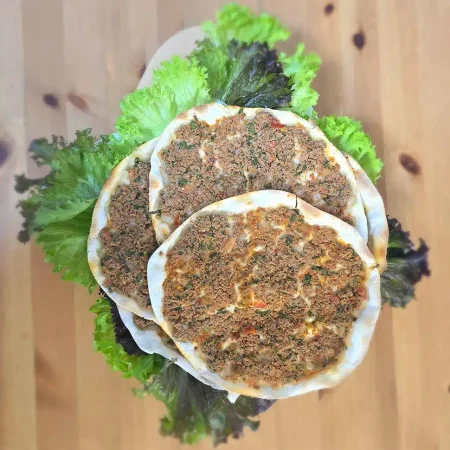 Teigfleisch Frisch gebackenes Hackfleisch (Lahm bi Ajeen) – dünner Teig belegt mit würzigem Hackfleisch, Petersilie und Tomaten, angerichtet auf grünem Salat.