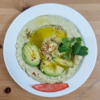 Cremige Avocado Meze ohne Kichererbsen mit Olivenöl, garniert mit frischer Minze und Avocado-Spalten – serviert von Catering Aleppo Berlin.